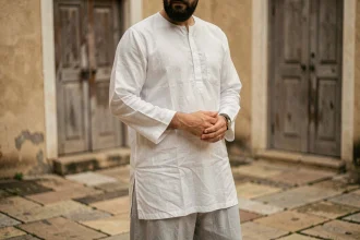 Homme musulman portant un sarouel gris clair et une tunique blanche dans une cour en pierre, tenue islamique confortable et pudique