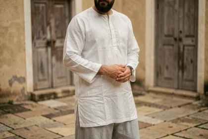Homme musulman portant un sarouel gris clair et une tunique blanche dans une cour en pierre, tenue islamique confortable et pudique